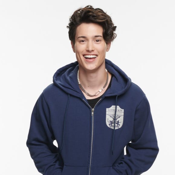 A young man wearing a blue zip up hoodie with a grey Godolkin crest printed on the left breast.