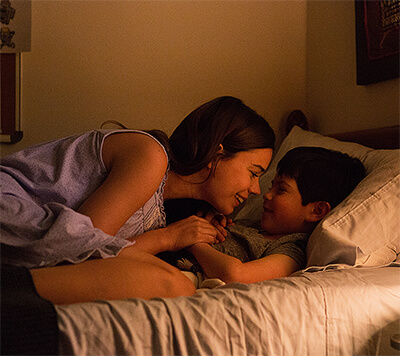 Isabel rubs noses with her child as she tucks them into bed.