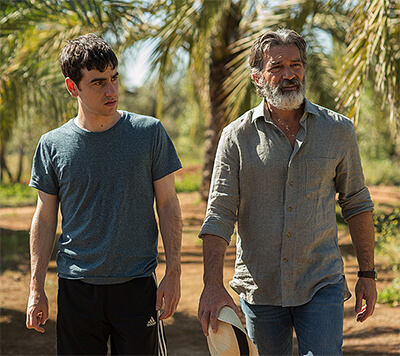 Mr. Saccione and Rodrigo take a sunny but stoic walk together through a garden of palm trees.