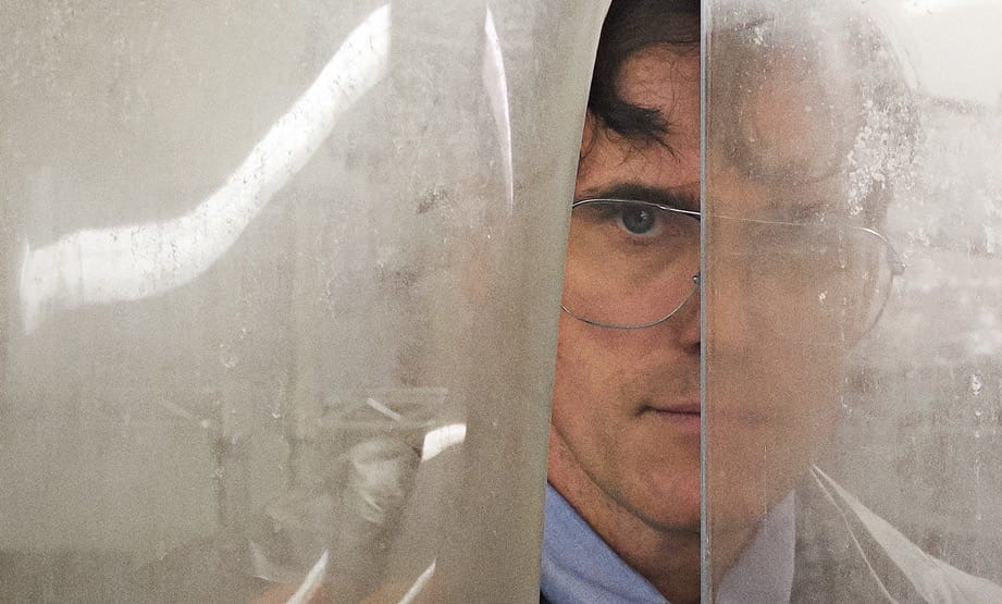 Matt Dillon playing Jack wearing a suit and glasses and peeking through a plastic curtain.
