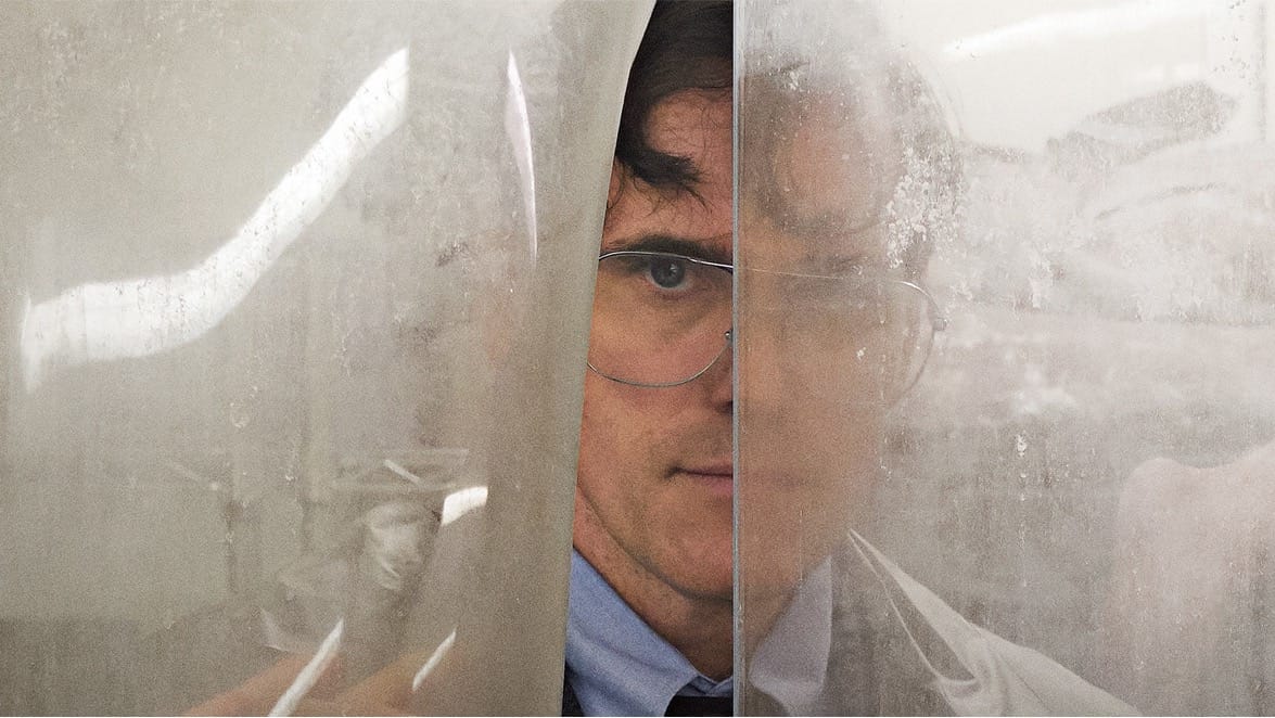 Matt Dillon playing Jack wearing a suit and glasses and peeking through a plastic curtain.