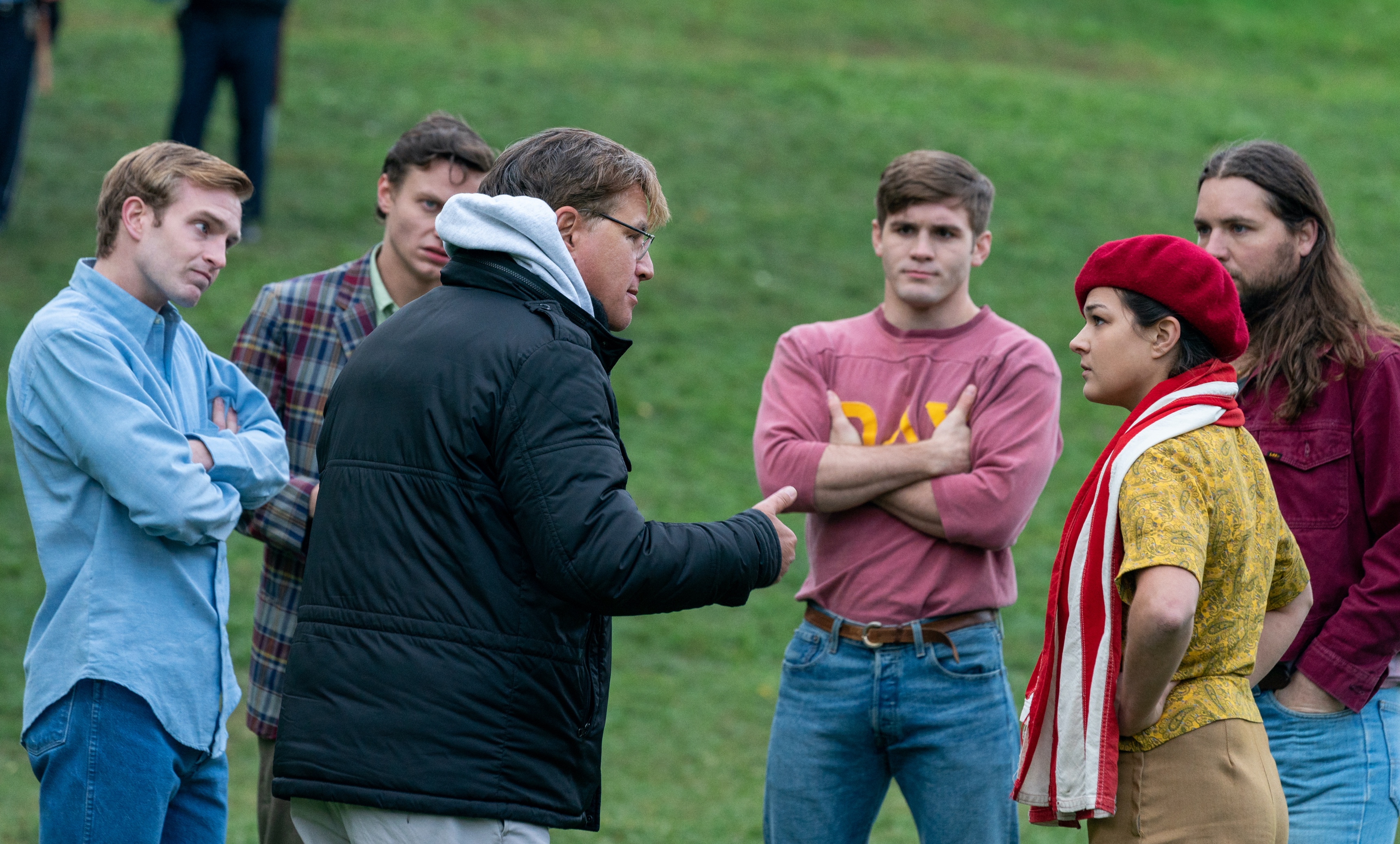 Extras circle around Aaron Sorkin as he prepares them for a protest scene in The Trial of the Chicago 7.